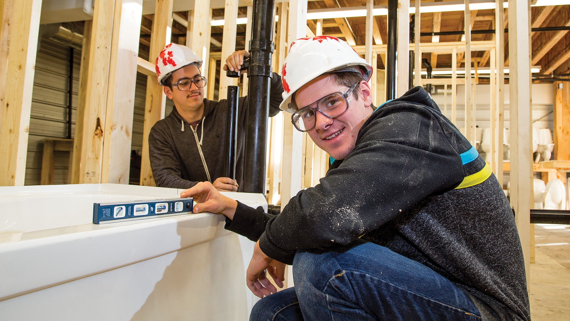 Two piping trades students fitting pipes in a room full of wooden beams.