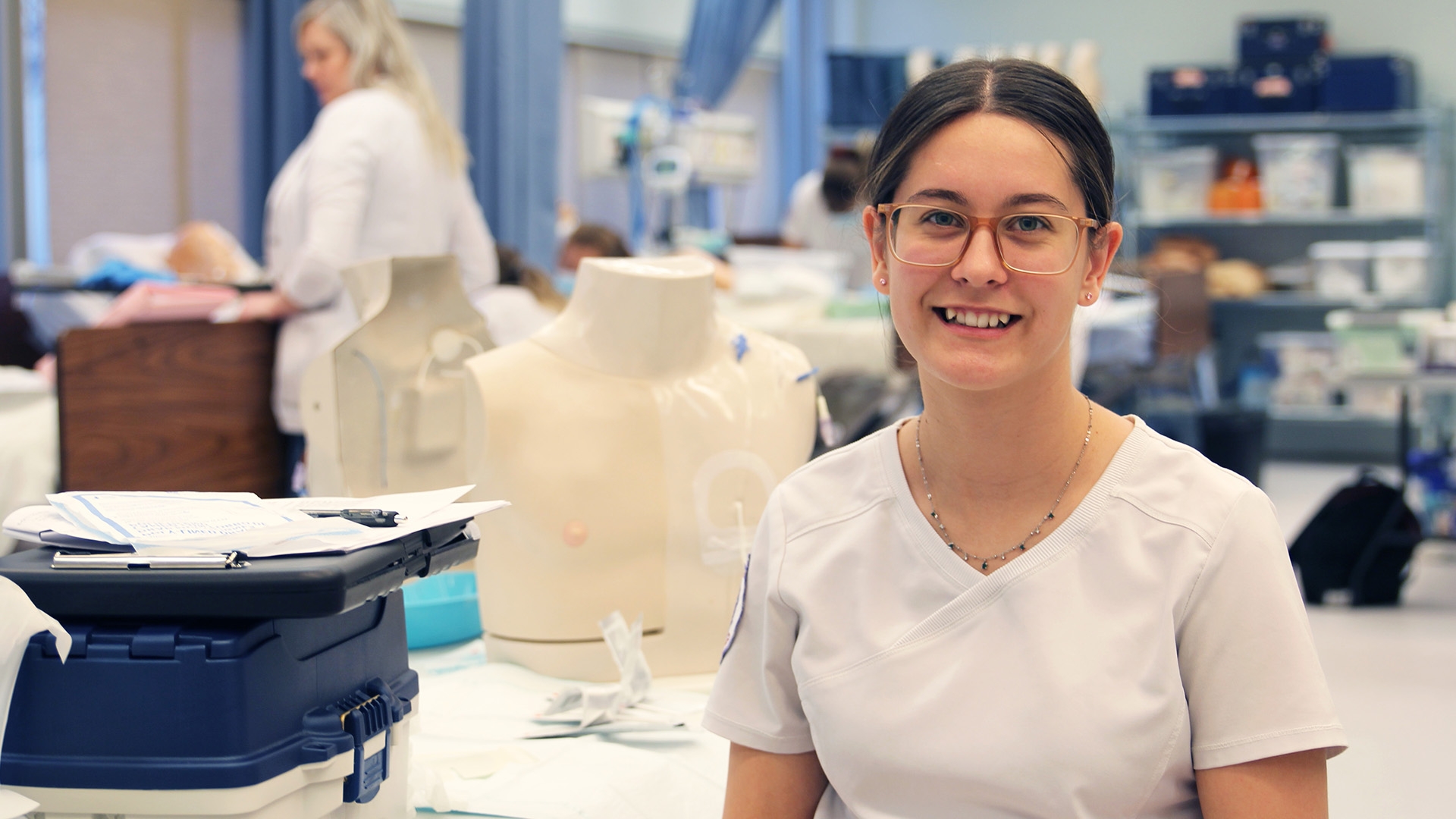 Practical Nursing student sitting next to a desk with nursing supplies in Assiniboine's HOLO suite.