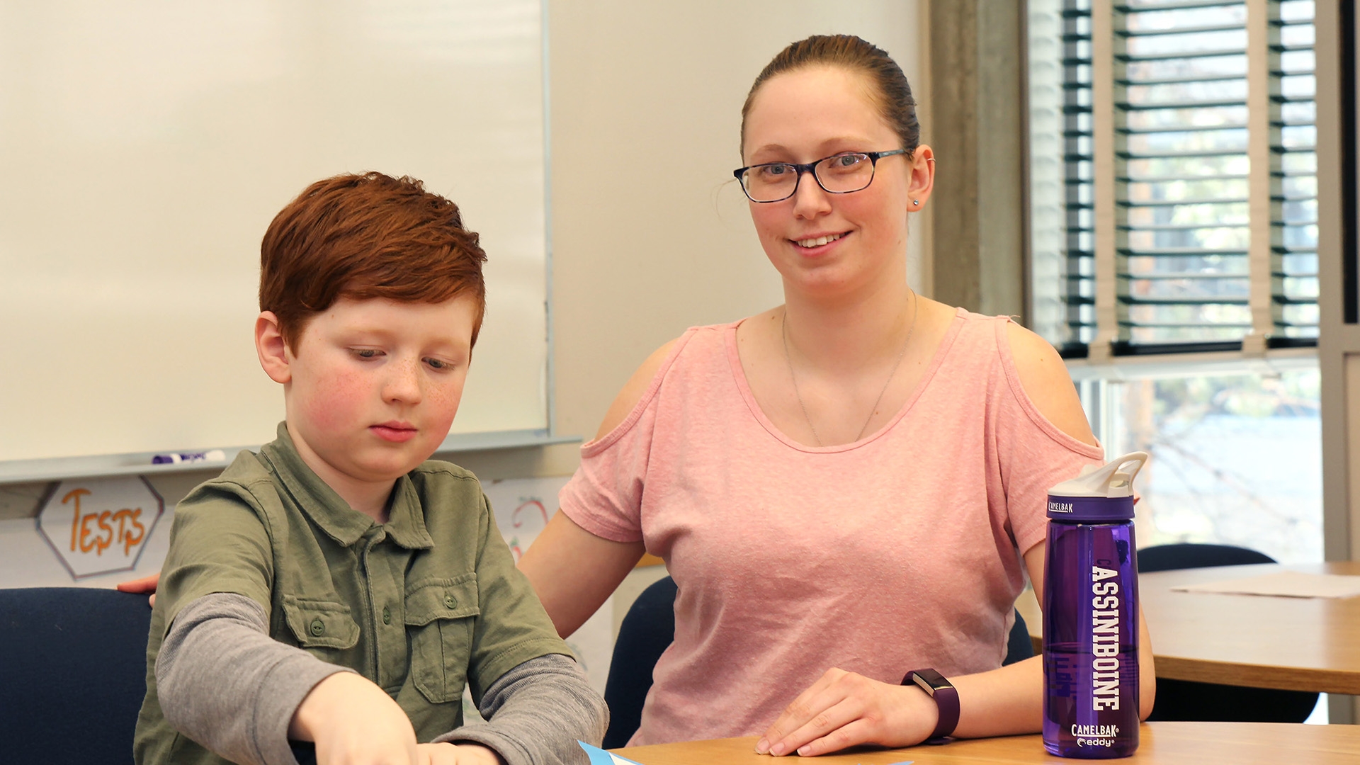 An education assistant sitting next to a boy in a classroom.