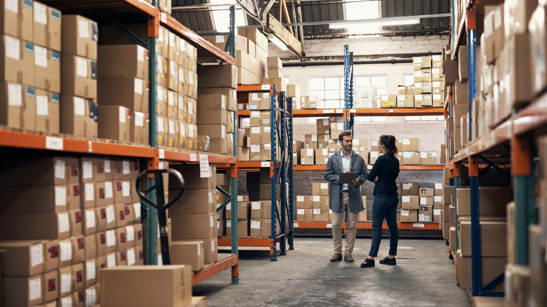 Two people standing in a storage facility surrounded by tall shelves filled with boxes.