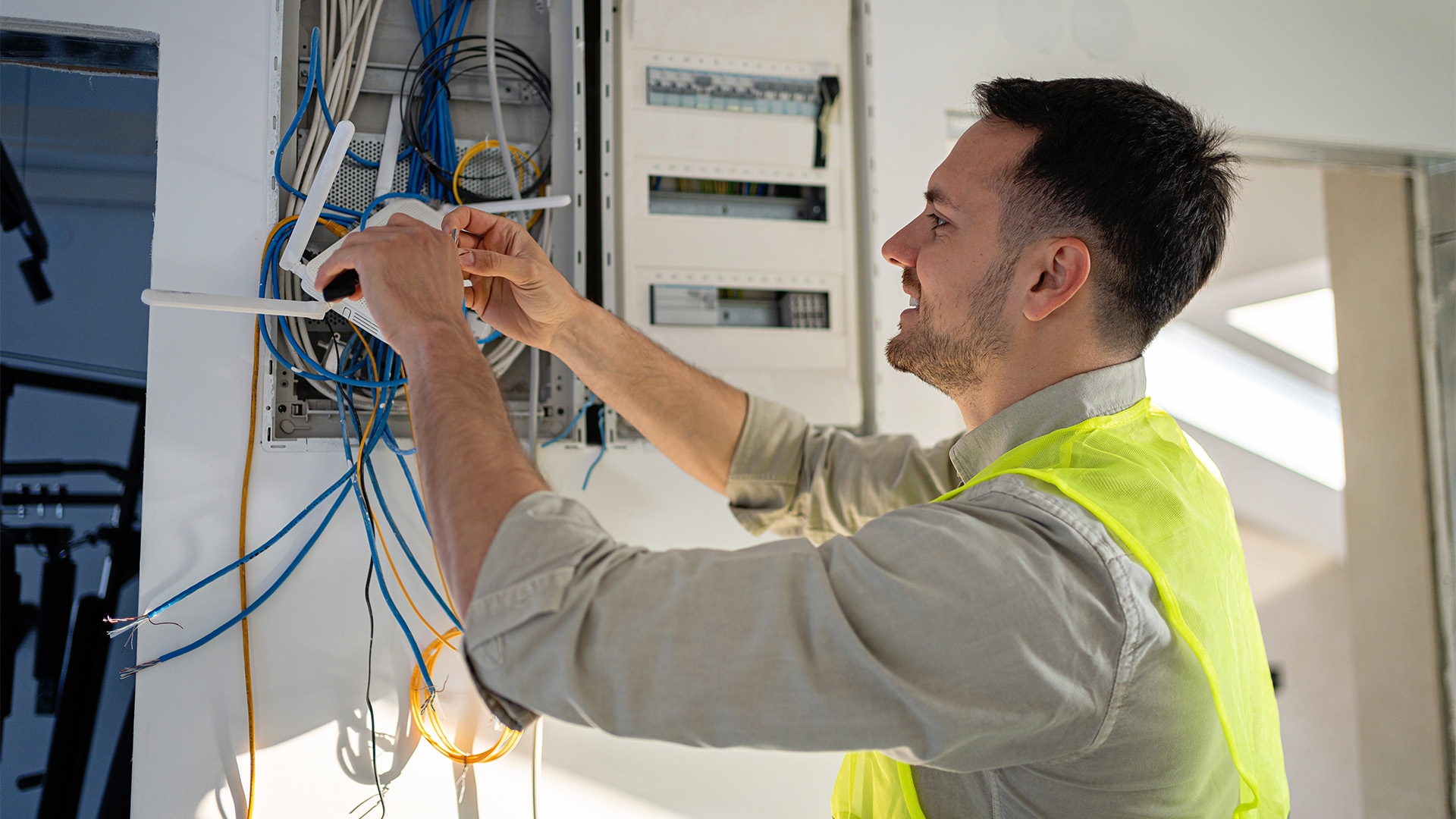 A male technician in a high visibility vest installing a router.