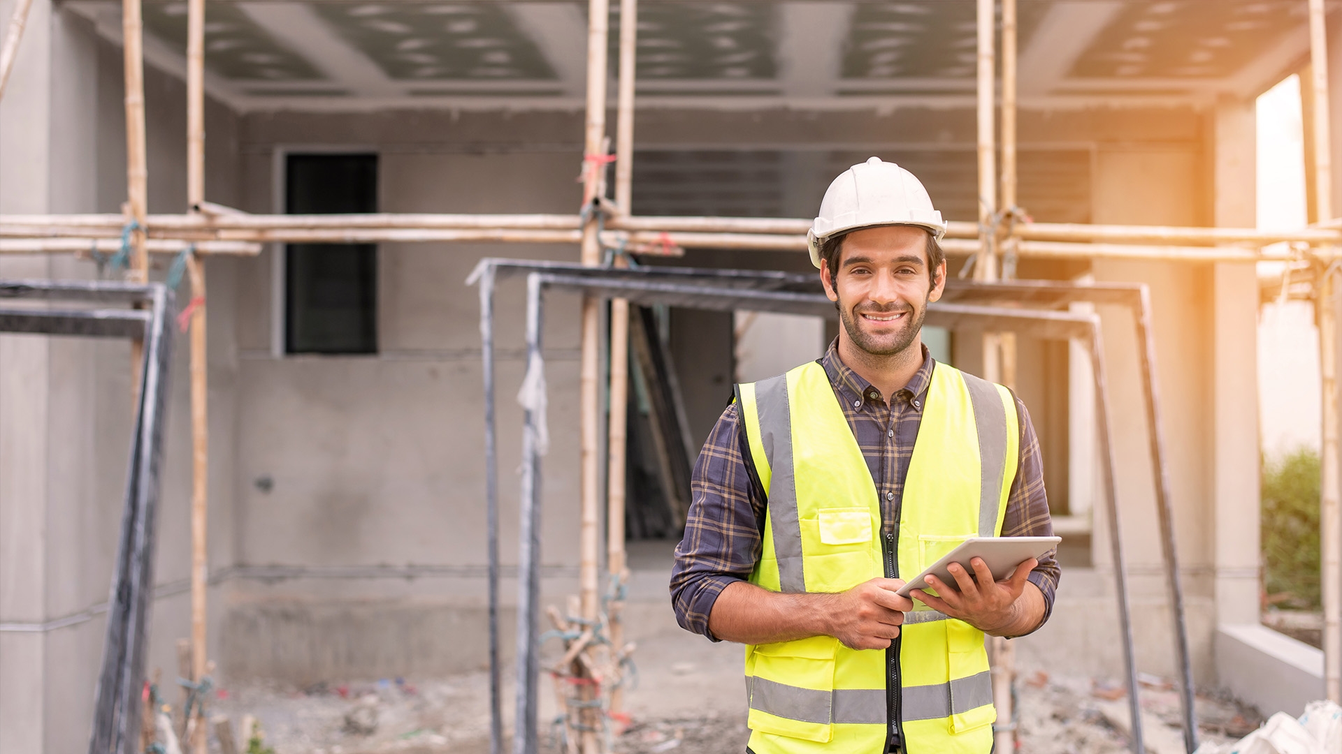A man in a high visibility vest and a hard hat standing in front of a scaffolding.