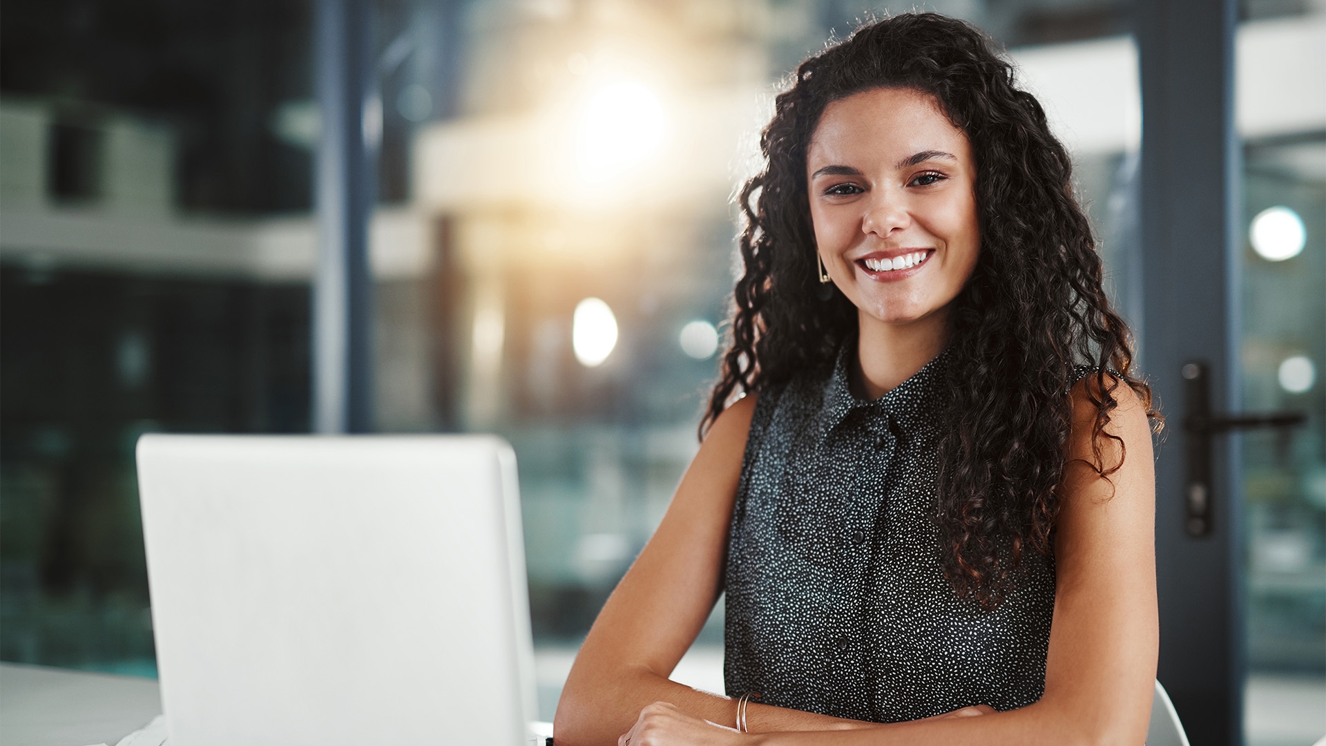 A woman sitting in an office in front of a laptop, smiling.