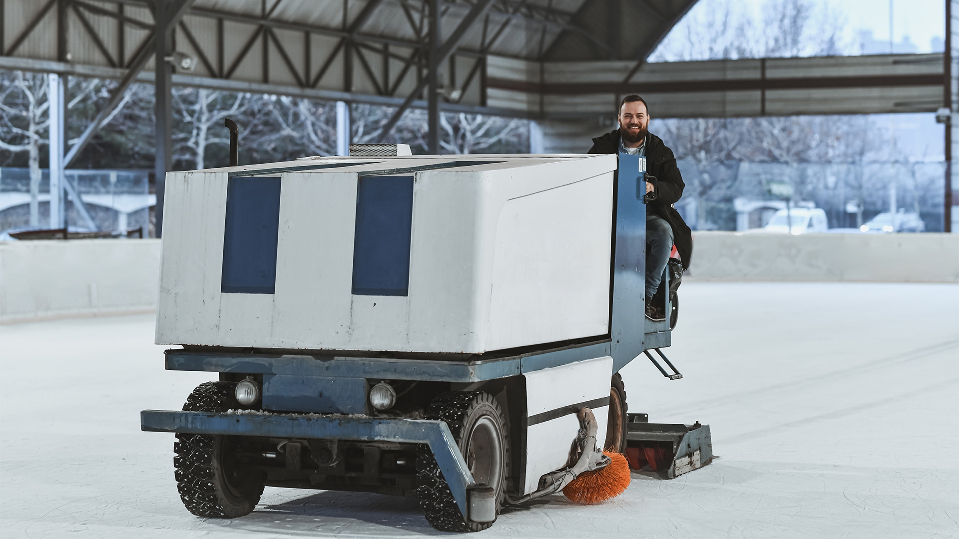 Ice facility worker driving a zamboni machine on a rink.