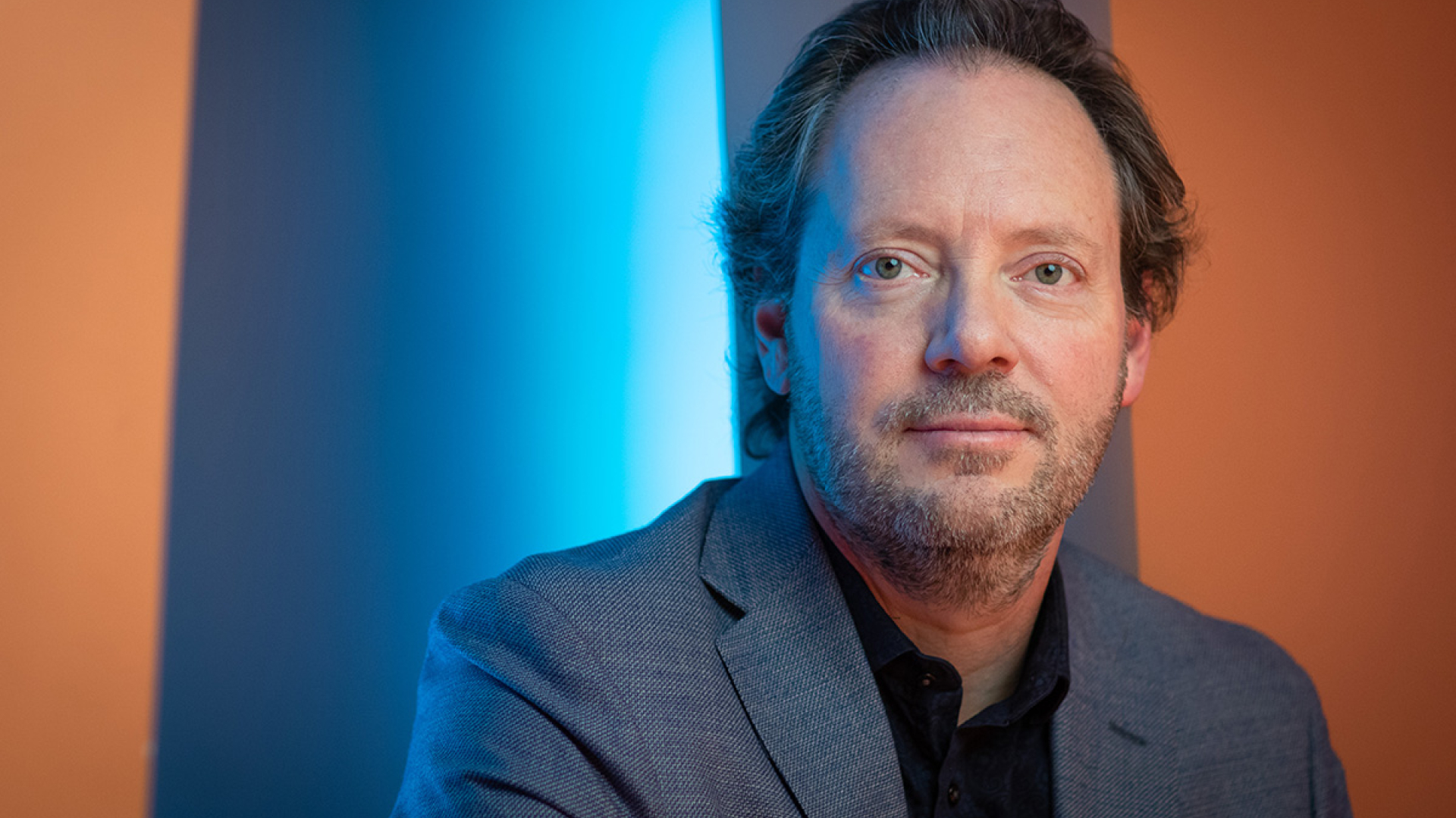 Brad Mahon portrait photo with a blue, grey and orange background.