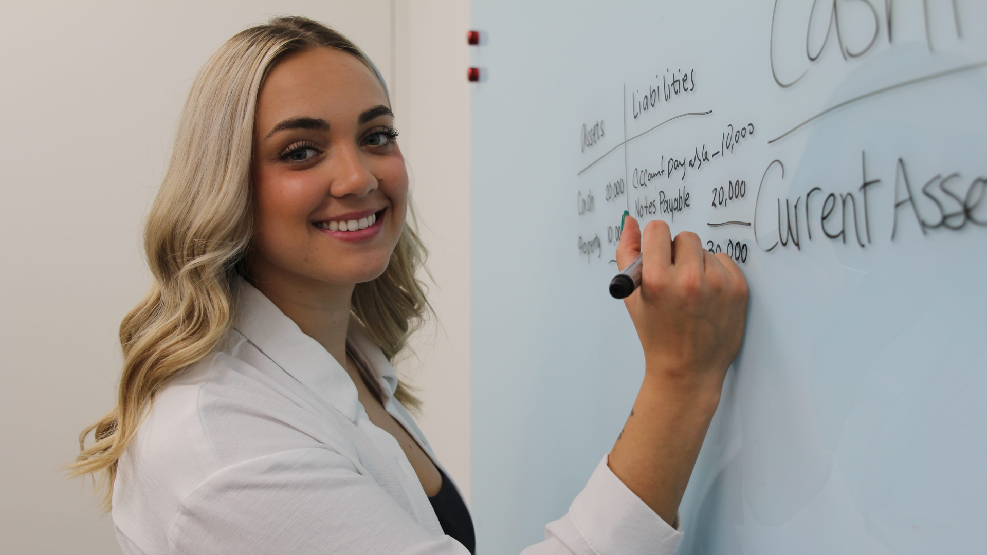 Female writing on board while smiling at the camera