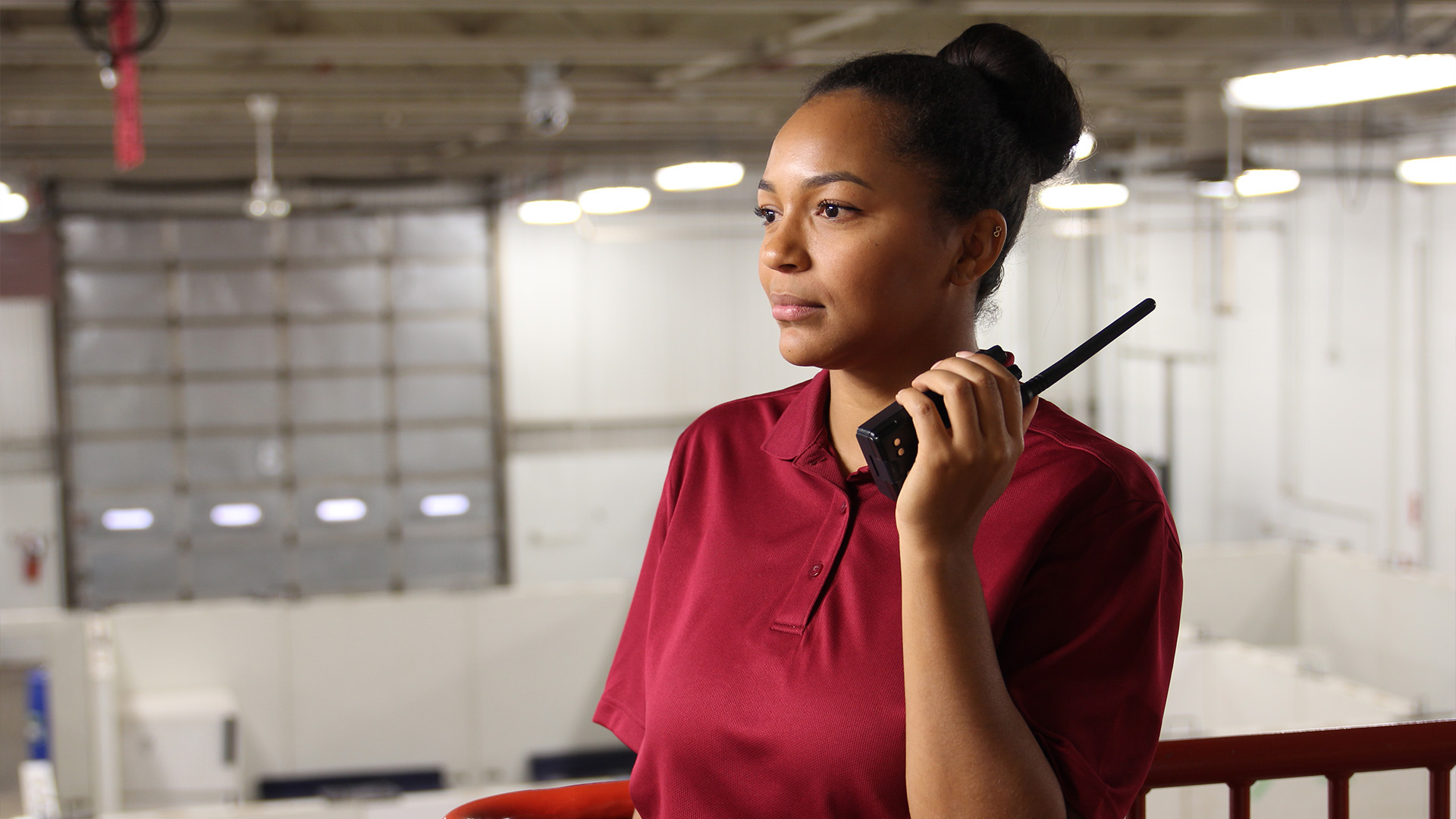 A Public Safety student in a red polo shirt standing on top of a staircase in the training centre, holding a radio.