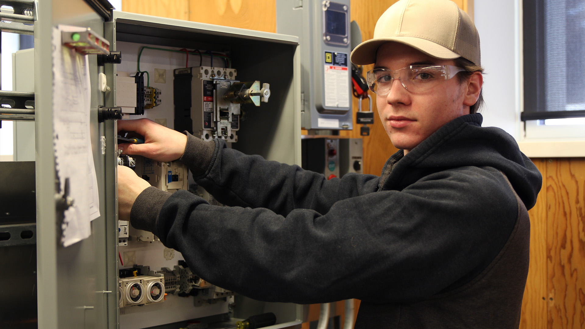 Construction electrician student standing in front of an electrical box, adjusting the wiring.