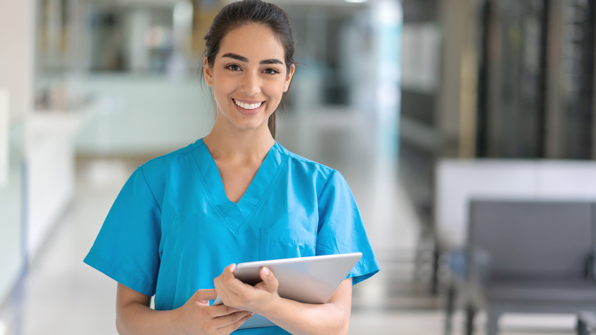 A nurse in blue scrubs standing with a tablet.