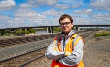 Jonn Olson standing in a high visibility vest with railroad tracks spanning in the background.