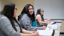 A row of students taking notes during class, one looking at the camera.