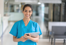 A nurse in blue scrubs standing with a tablet.