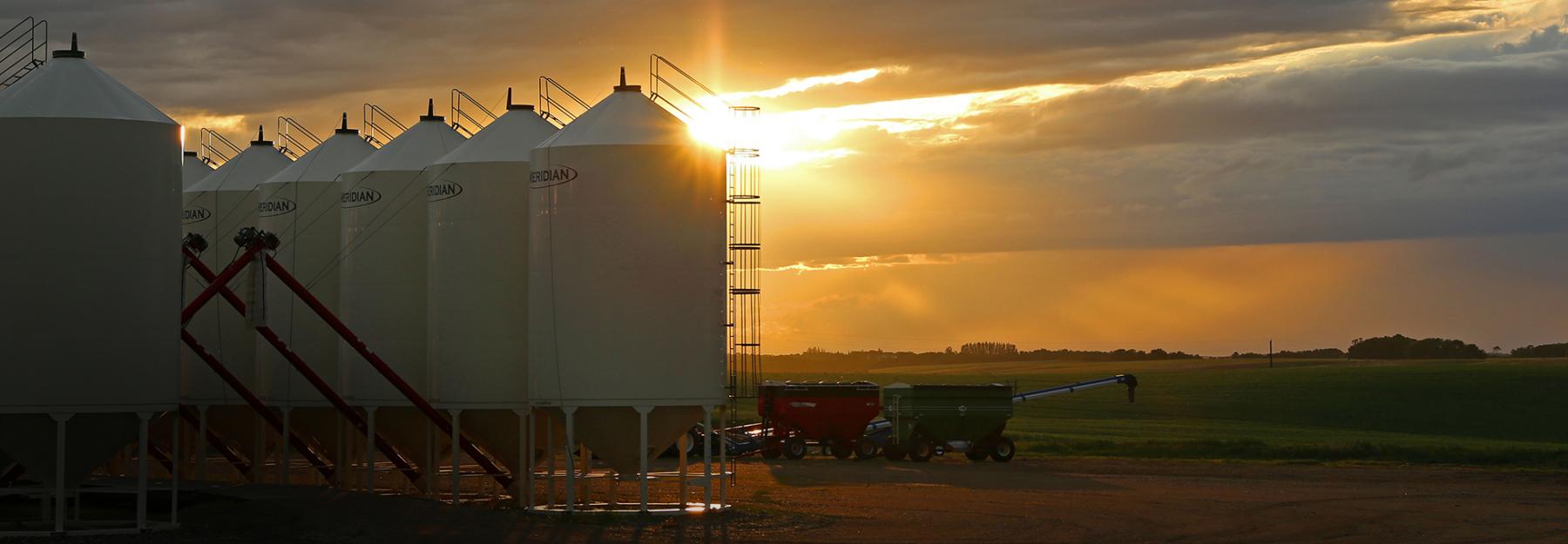 Grain bins and farm equipment at sunset