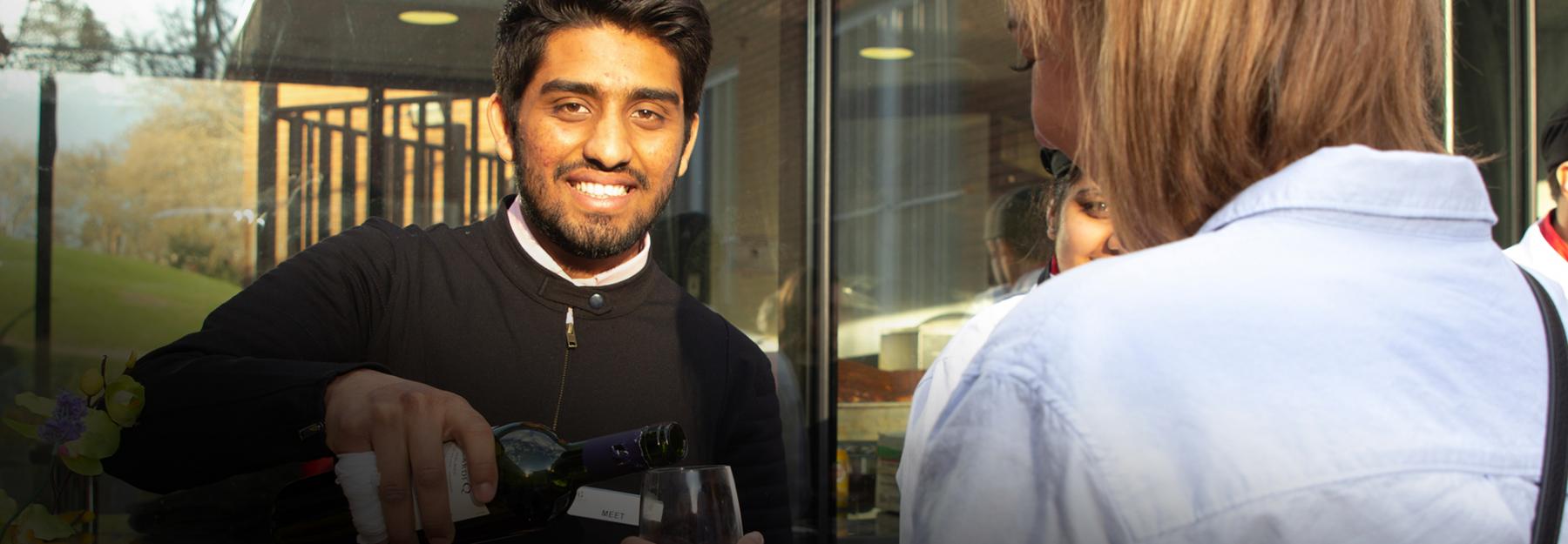 Hotel & Restaurant Management student serves wine to a guest
