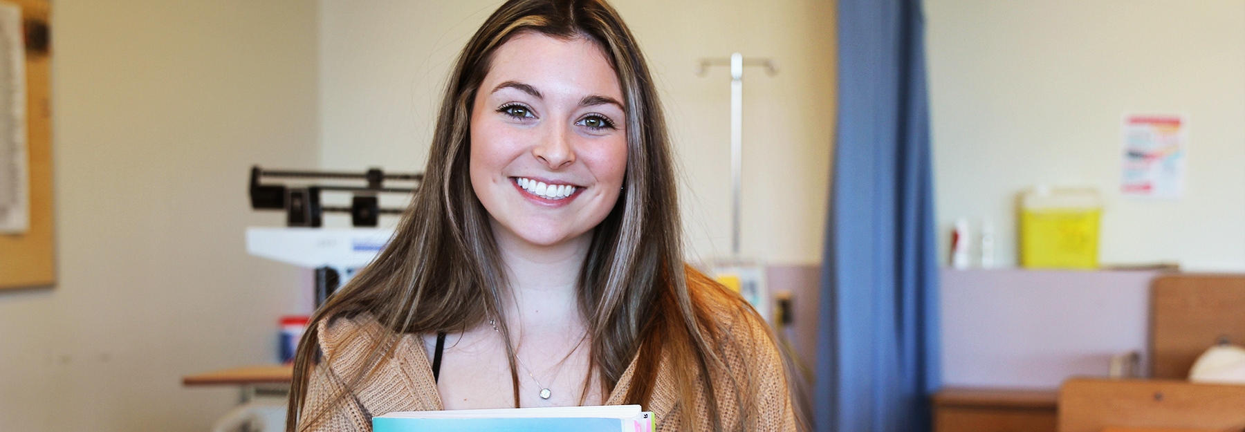 A female student standing in a classroom, holding a book.