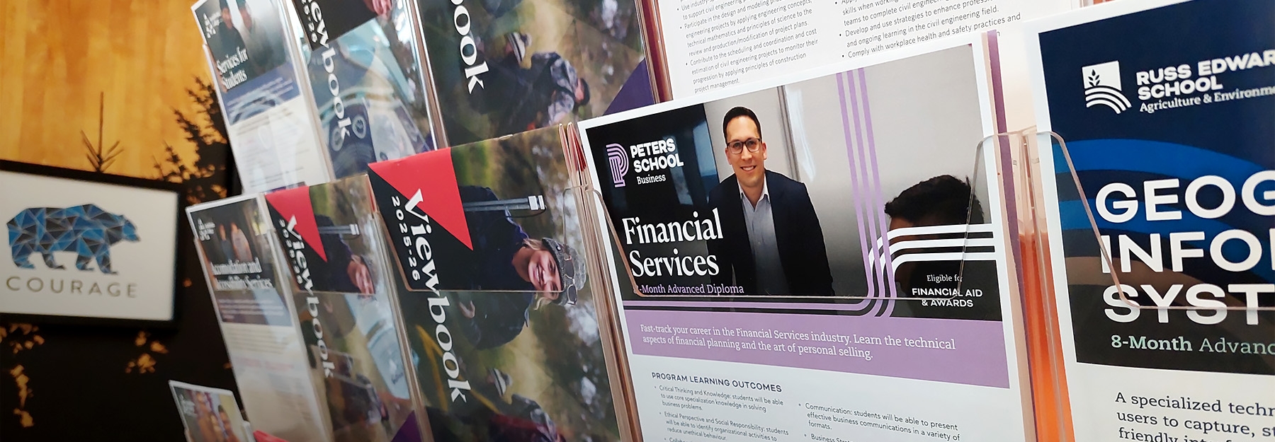 A wall filled with Assiniboine College publications, with a close-up on a Financial Services sheet.